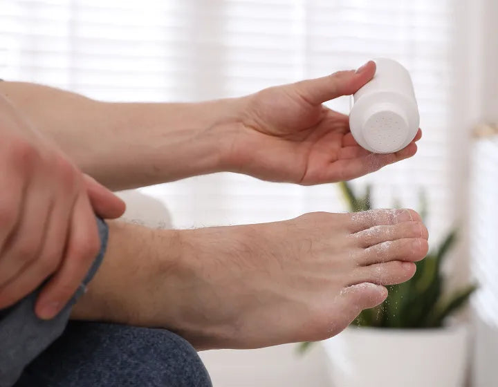 Person applying powder to their foot with a small container.