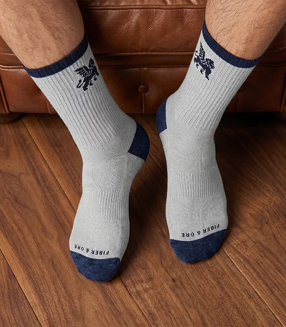 White socks with blue accents worn by a person sitting on a brown leather couch.