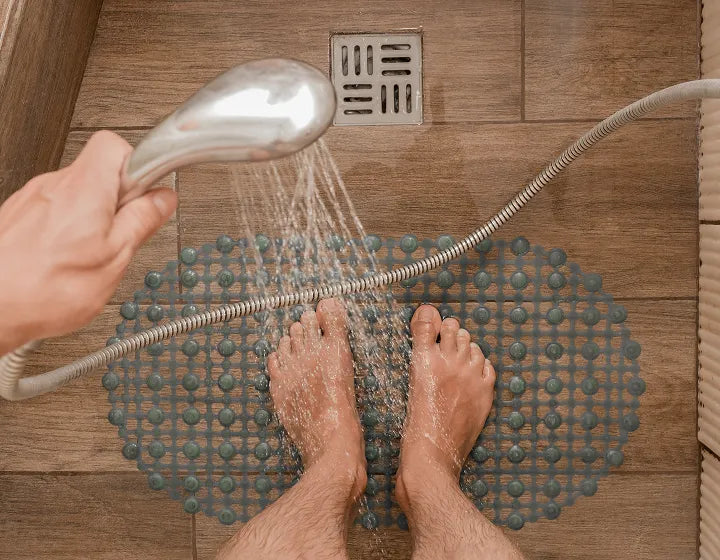 Person using a handheld showerhead on a textured mat in a shower.